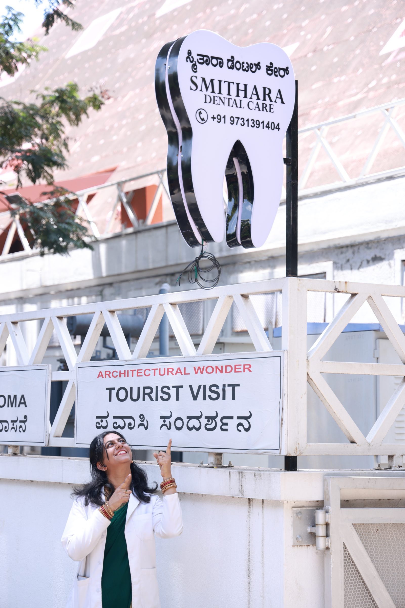 Dr. Sushmitha pointing up at the Smithara Dental Care signboard outside the clinic